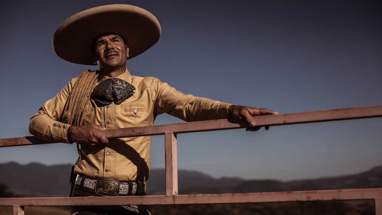 Charro in a wide sombrero leaning on a fence in the hills near Compostela, Mexico